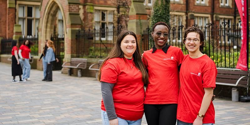 Three smiling student ambassadors in red t-shirts stand together outside Clothworkers Court.